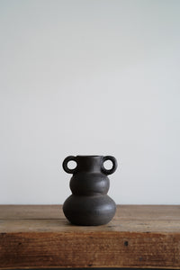 A hand sculpted clay vessel with dramatic curves and a matte black finish