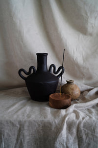 This handmade rustic vase with unique curved handles and a dark chocolate brown finish. Paired here with our small mud vase and wooden incense holder